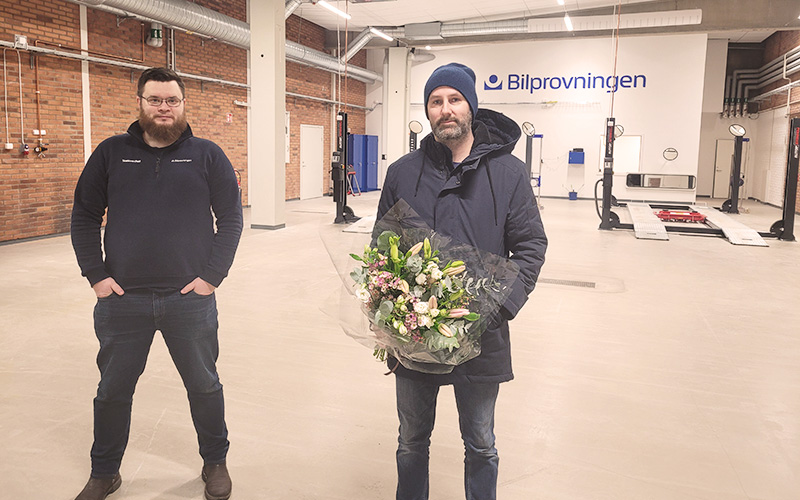 Bilprovningens stationschef ger en kund blommor i besiktningshallen på den nya stationen i Jakobsberg.