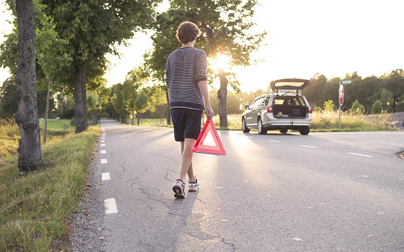 En ung man placerar en varningstriangel på vägen framför en havererad bil. 