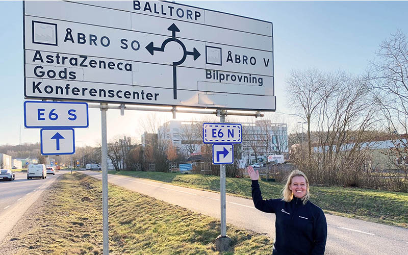 Kvinnlig bilprovningsanställd pekar på en vägskylt vid Åbro, Mölndal