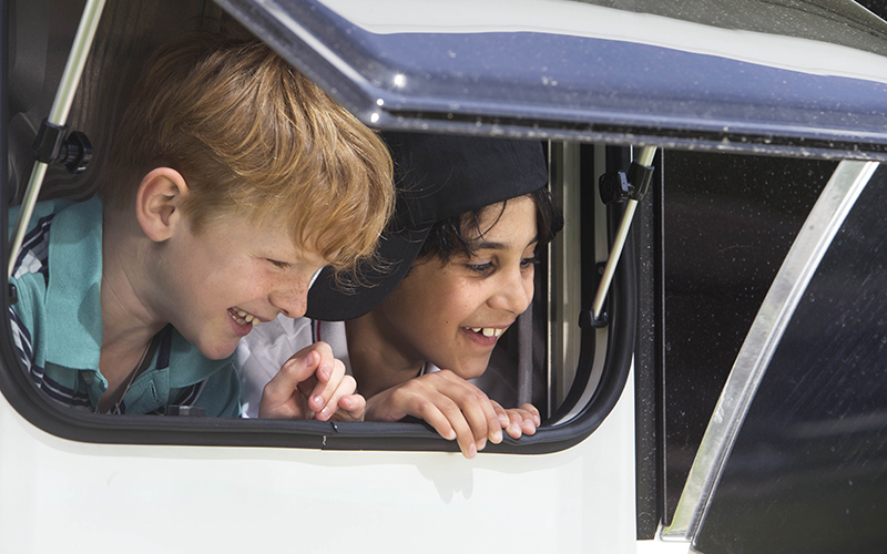 Två glada pojkar som tittar ut ur ett fönster på en husbil