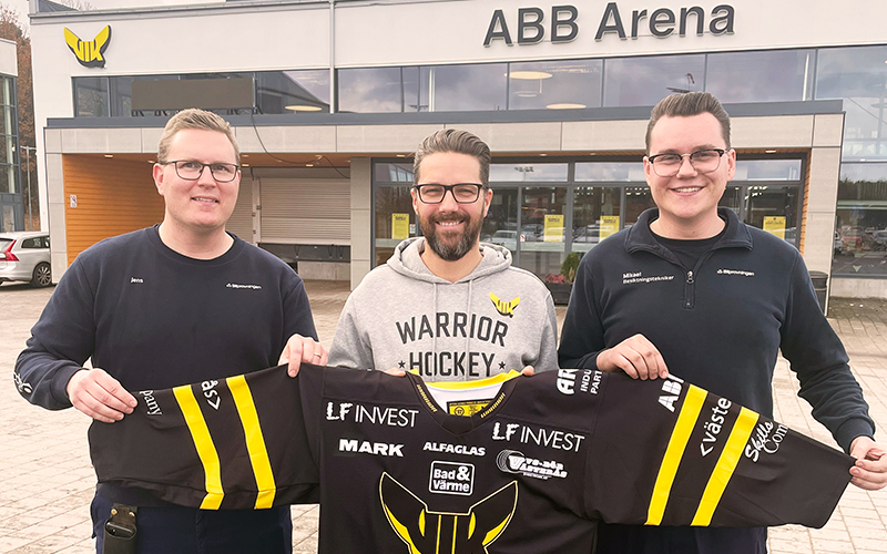 Tre leende killar - två från Bilprovningen och en från Västerås IK - står framför ABB arena och håller en hockeytröja. 